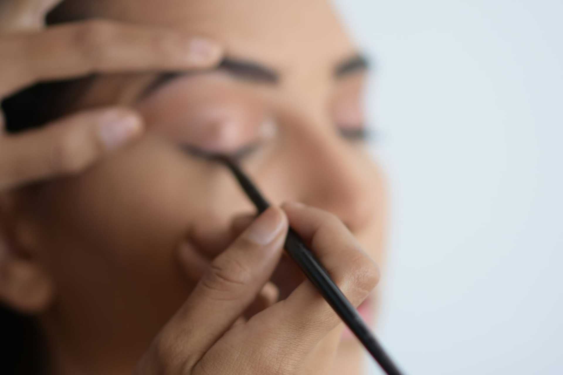 Applying eyeliner to closed eyelid with precision using a makeup brush.