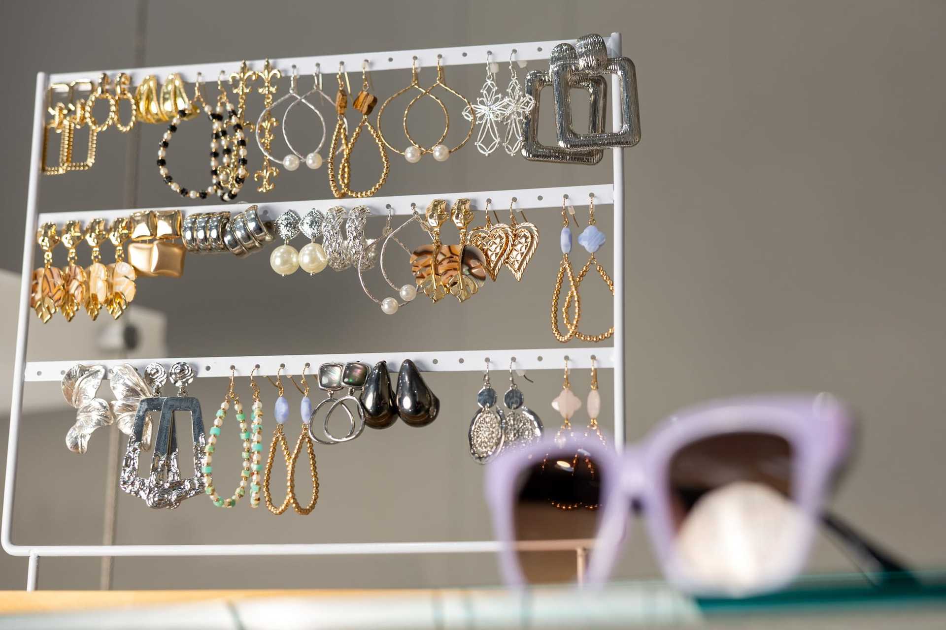 Rack of assorted earrings with blurred purple sunglasses in the foreground.